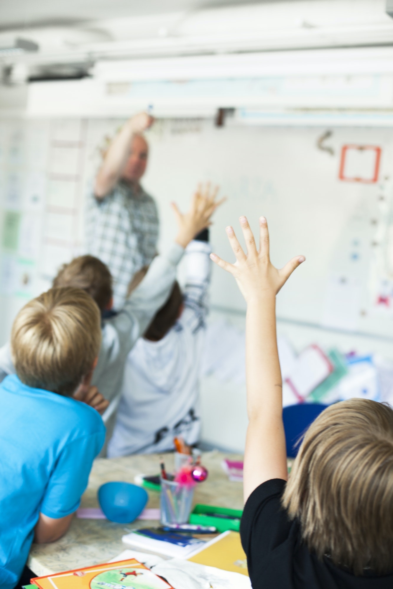 Rear view of children raising hands in classroom